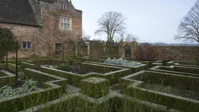 A winter day in the White Garden, with rectangular flowerbeds enclosed by neat hedging, and the red-brick house behind, at Sissinghurst Castle Garden, Kent